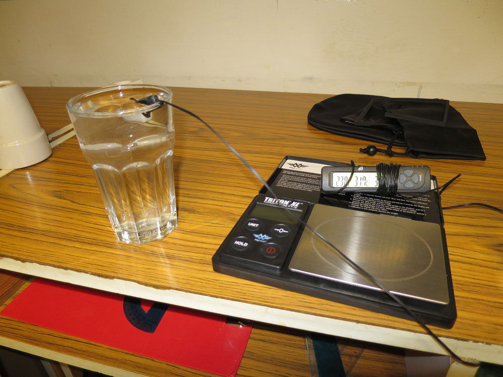 Experimentálna aparatúra: pohár s vodou a digitálna váha. Teplota vody je práve meraná digitálnym teplomerom